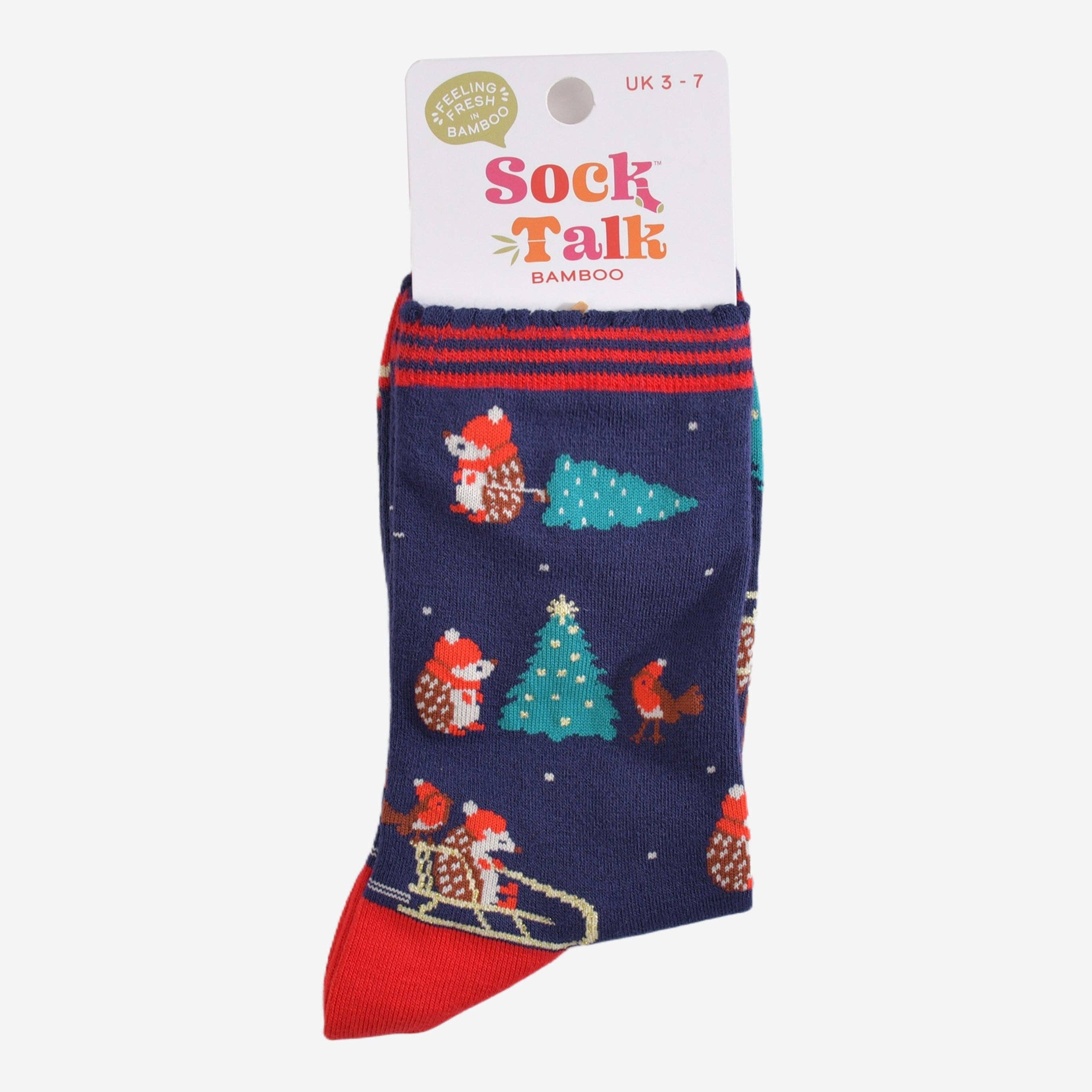 Et par mørkeblå julesokker med pinnsvin på en slede og juletrær, pakket sammen i sin originale emballasje med merkets navn "Sock Talk".






