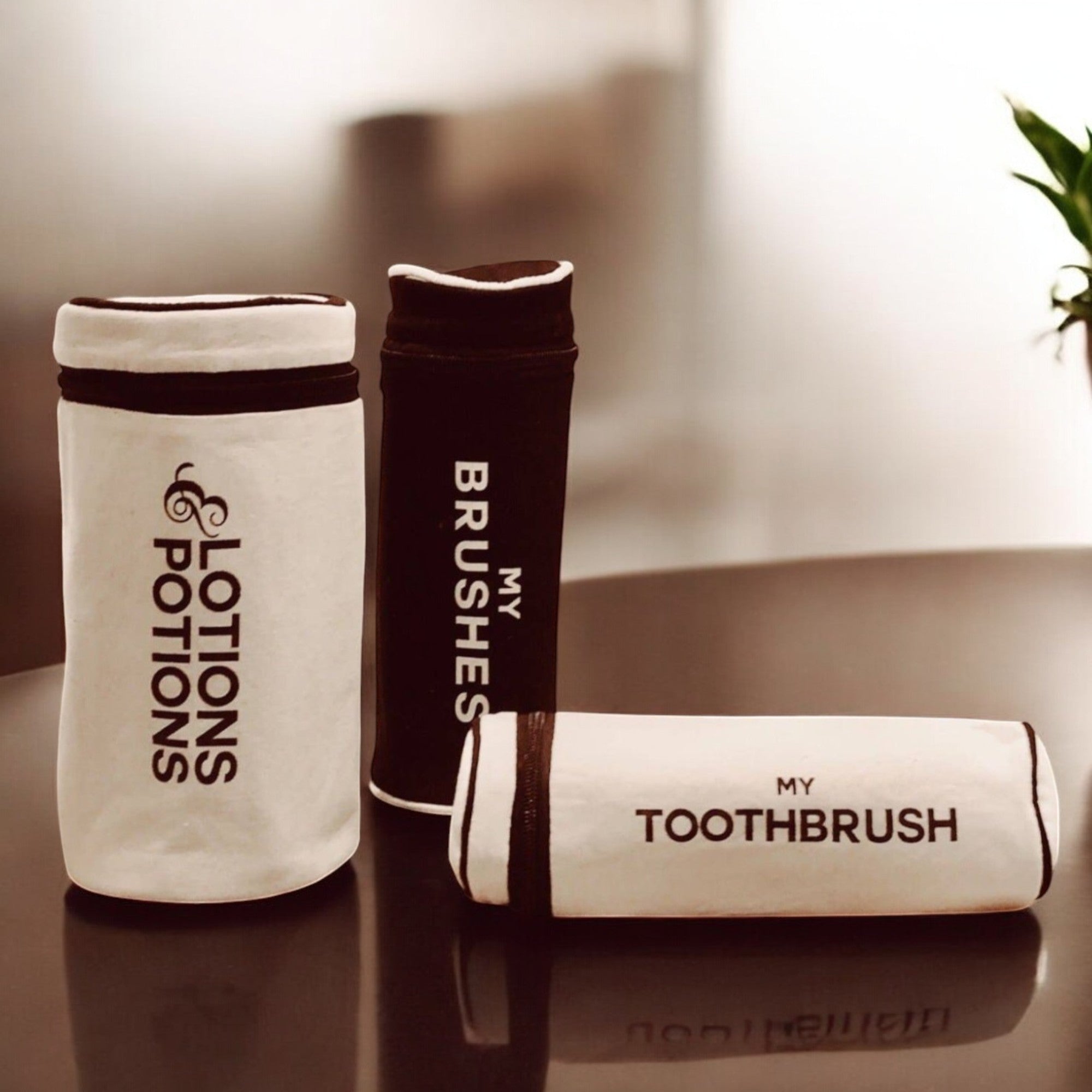 Tannbørsteetui og toalettholdere i sort-hvitt design med teksten 'My Toothbrush,' 'My Brushes,' og 'Lotions & Potions,' plassert på et bord med en minimalistisk bakgrunn.